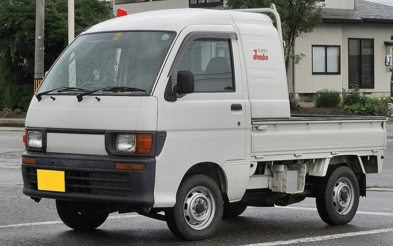 White Daihatsu Hijet Super Jumbo 4WD kei truck with the extended cab, parked on a street