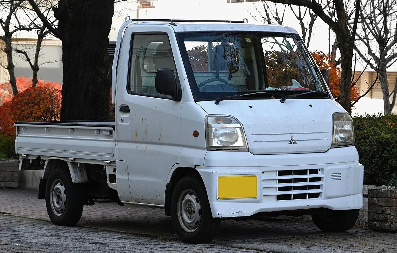 White 1999 to 2000 Mitsubishi Minicab Mighty kei truck with a flat bed, parked on a street