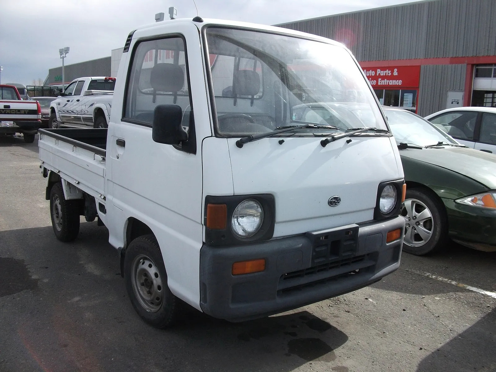 White early-1990s Subaru Sambar kei truck parked outside an auto parts store in Canada